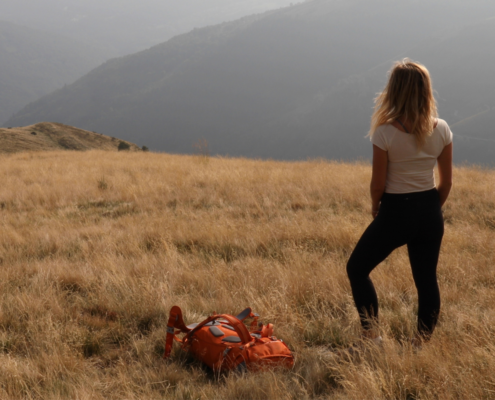 Female hiker sets backpack down on grassy hillside feeling discouraged lighten your load