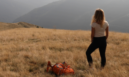 Female hiker sets backpack down on grassy hillside feeling discouraged lighten your load