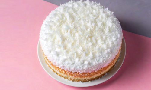 overhead angle of a coconut cake covered in white frosting and lots of shredded coconut on a midcentury countertop