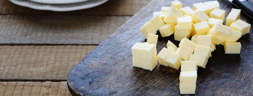 butter along side a knife that has cut it into small pieces sitting on a black cutting board