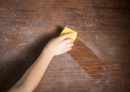 DIY dusting spray womans hand wiping dusty wood surface with yellow towel