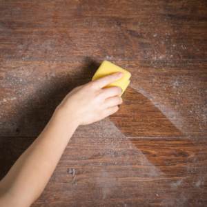 DIY dusting spray womans hand wiping dusty wood surface with yellow towel