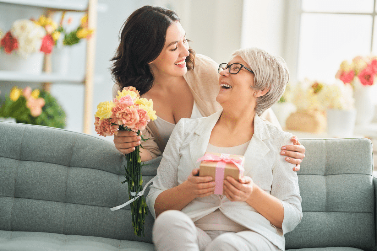 daughter hugging smiling mother with flowers in hand