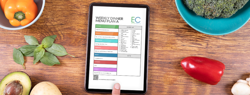 kitchen countertop with assorted fruits and vegetables and mobile tablet with weekly dinner menu plan