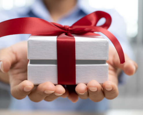egifting female hands holding white box with red ribbon passing gift