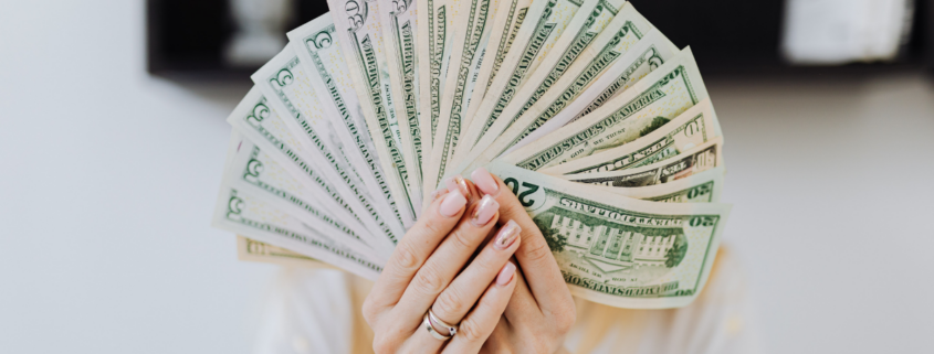 a financially confidence woman holding fanned dollar bills in hands covering face