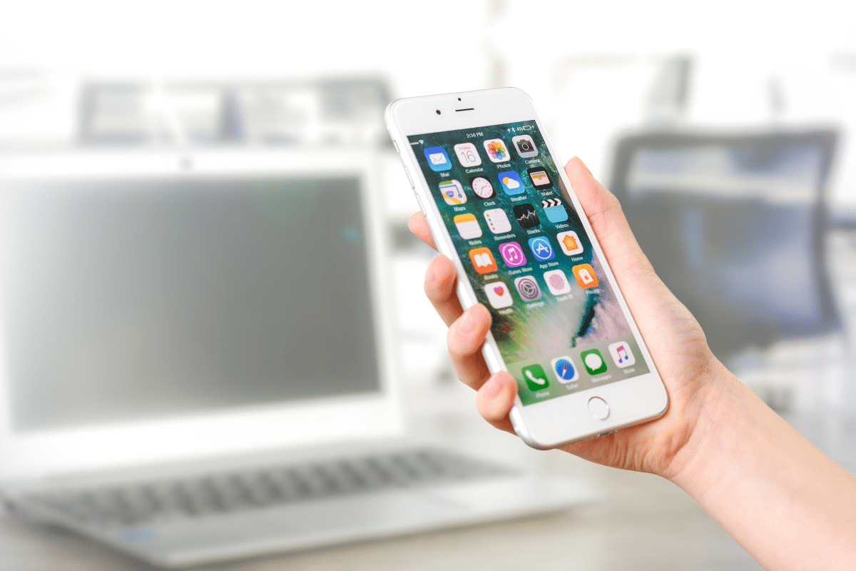 apple mail app on iphone woman's hand holding white device with laptop out of focus behind