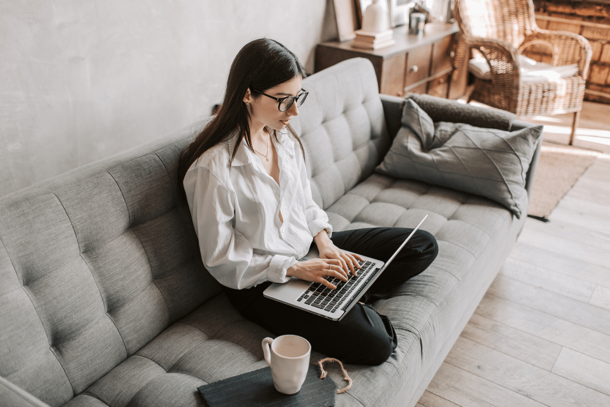young adult woman sitting cross legged on couch with laptop drinking coffee how to safelist email addresses