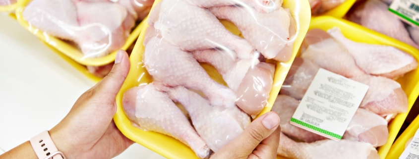 cost per serving grocery shopping woman holding package of raw chicken legs in front of refrigerated meat case