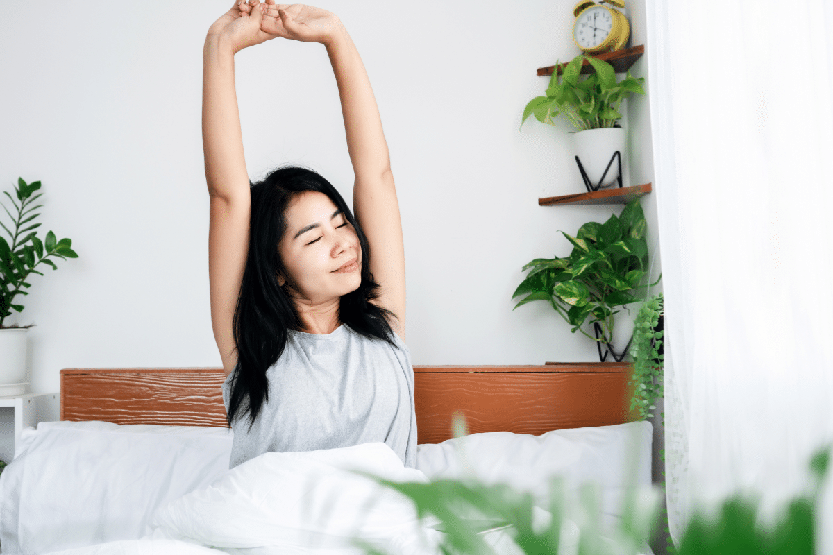 woman waking up in bed surrounded by plants happy healthy stretching arm