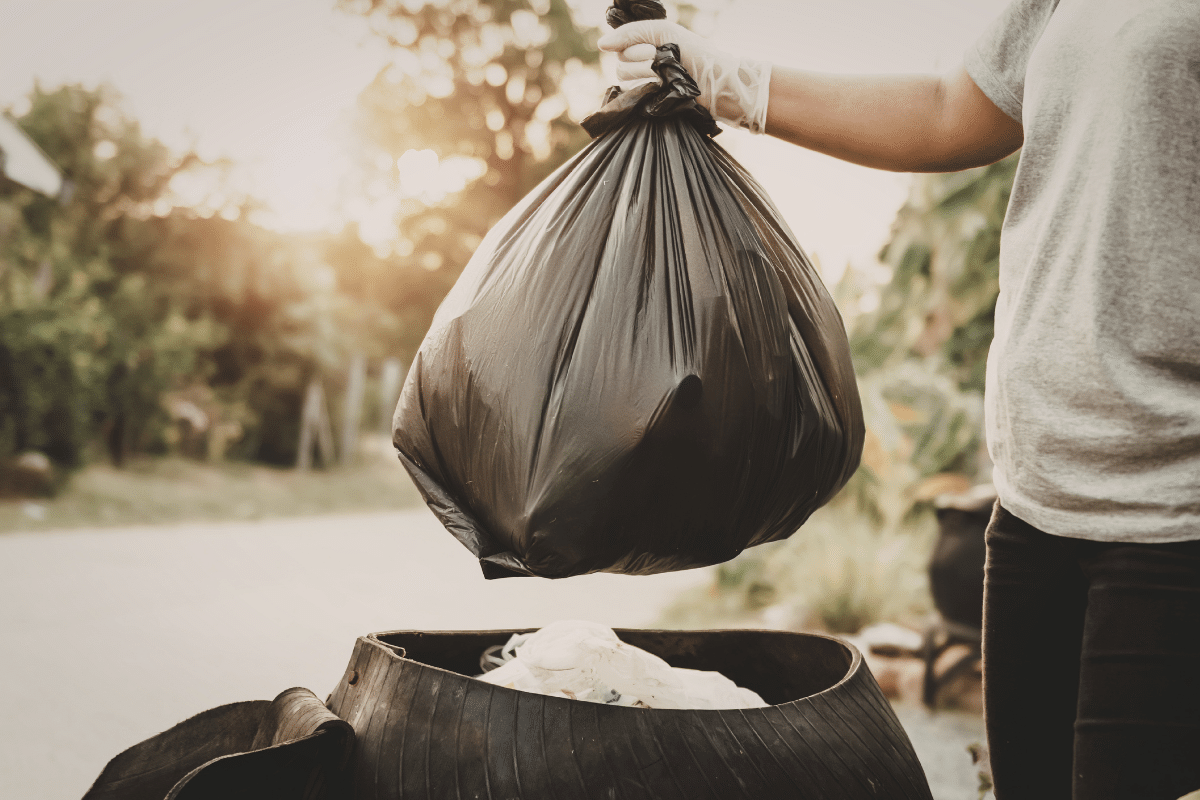 man throwing black trash bag away outside
