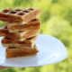 hand holding a white plate with a stack of belgian waffles with a blurred nature background