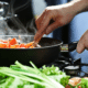 common kitchen mistakes woman stirring vegetales in a pan on the cooktop