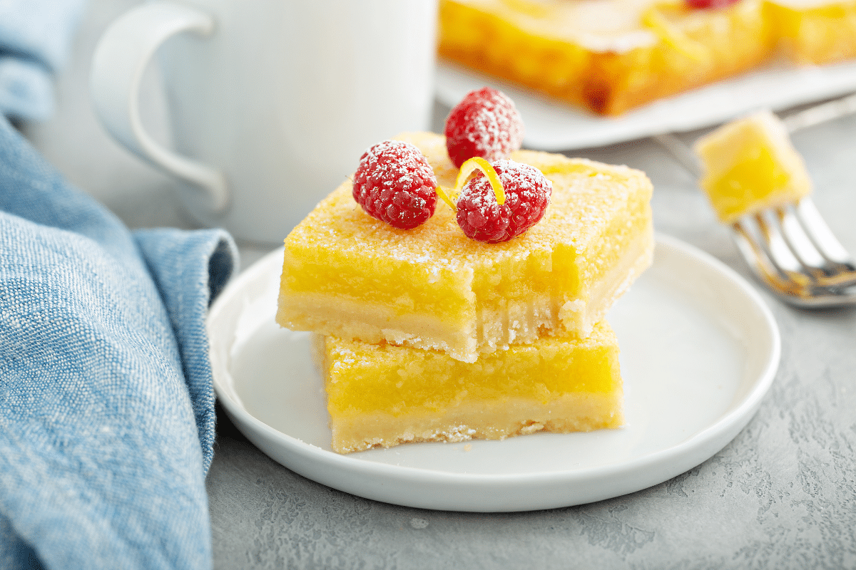 classic lemons bars on plate with raspberries on top