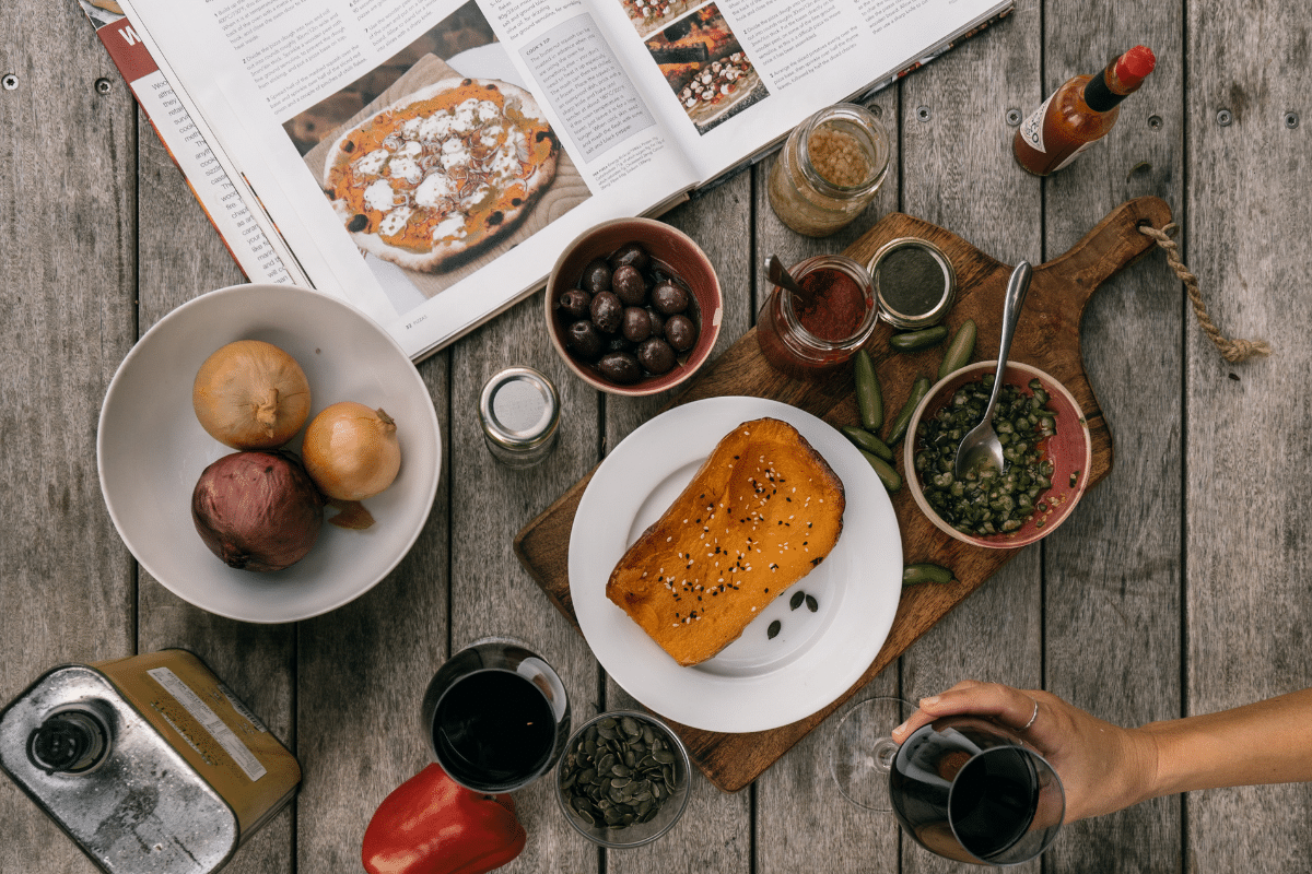 top view of kitchen countertop with recipe cookbook and ingredients glass of wine in woman's hand