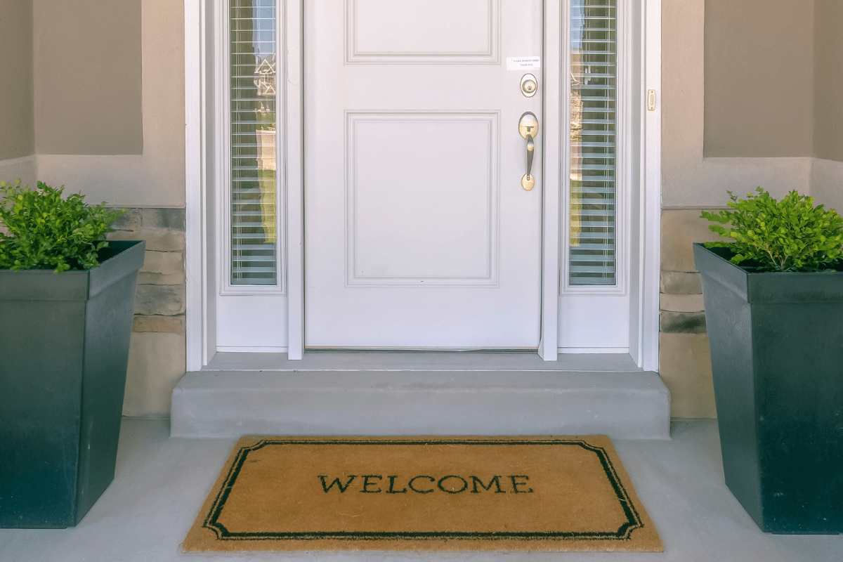 front door entry of home with welcome mat and plants for sale