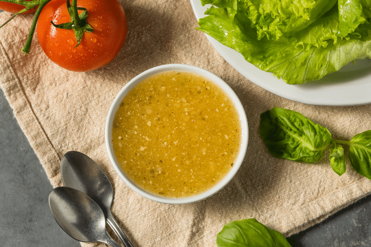 homemade italian dressing in a white bowl with fresh lettuce and a tomato