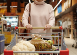 woman grocery shopping pushing cart with apples and cauliflower