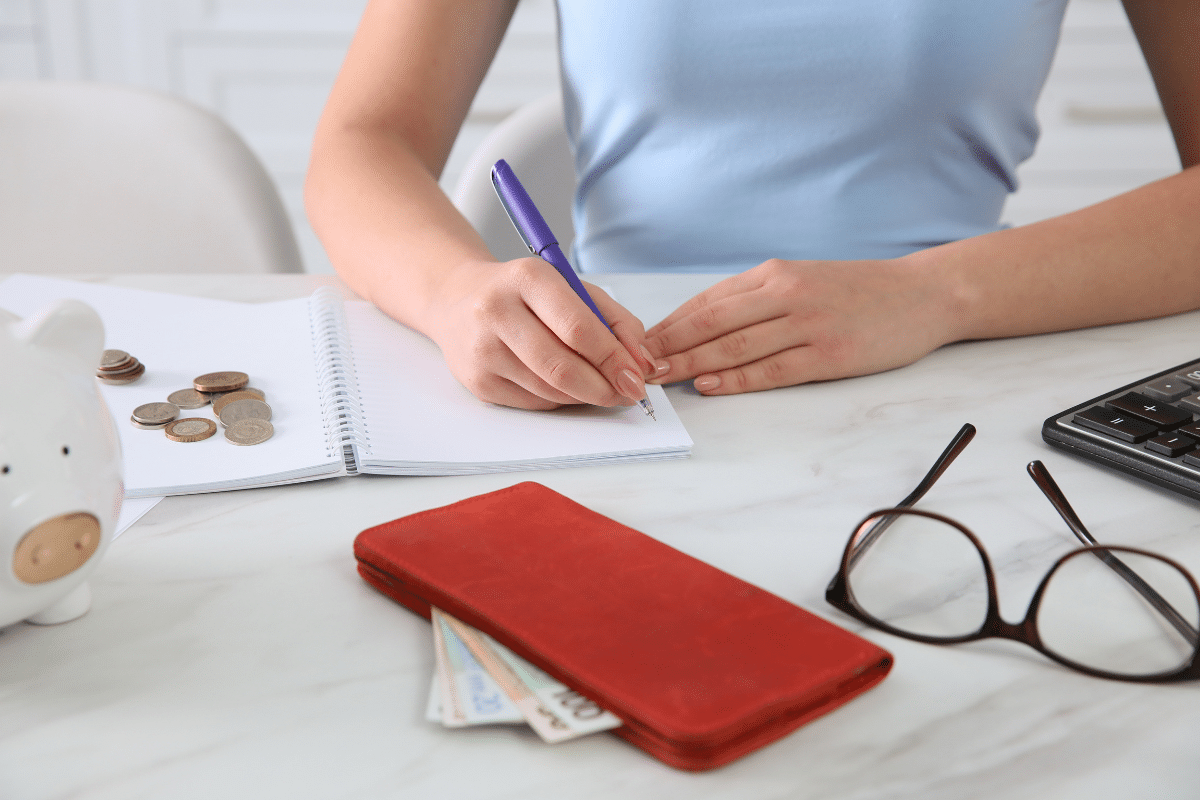 woman writing budget notebook kitchen table