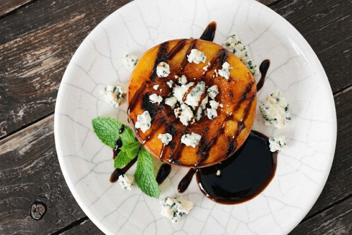 single serving of a grilled peach with balsamic and blue cheese dressing on a white plate