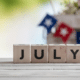 wooden die spell july with patriotic decor in background