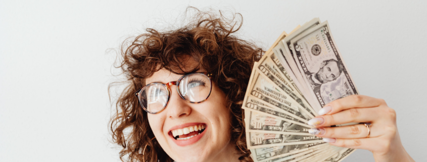woman holding a fan of money dollar bills smiling moneymaxxing