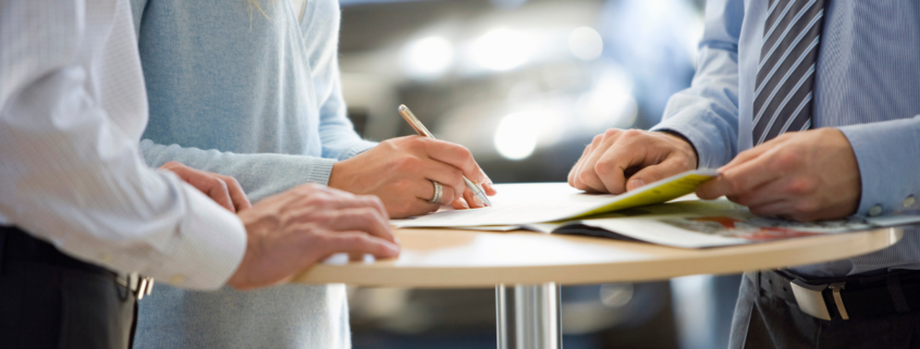 man and woman signing an extended warranty in a car dealership