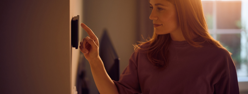 Woman Adjusting Smart Home Device on the Wall how to lower your electric bill
