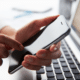 Woman using smartphone while checking monthly cellular data usage on laptop