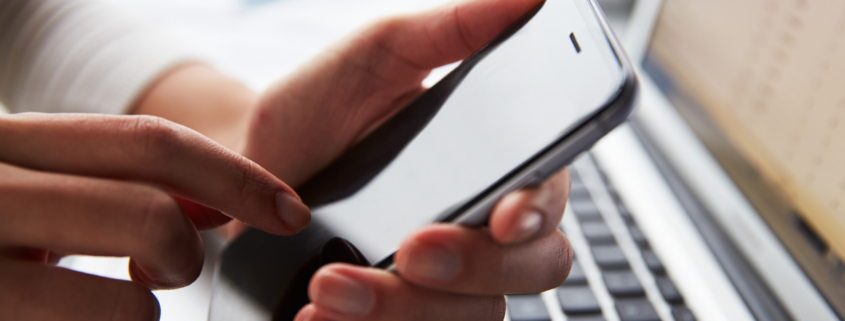 Woman using smartphone while checking monthly cellular data usage on laptop