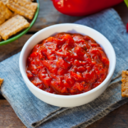Sweet pepper and onion relish in a white bowl with crackers and fresh red bell peppers