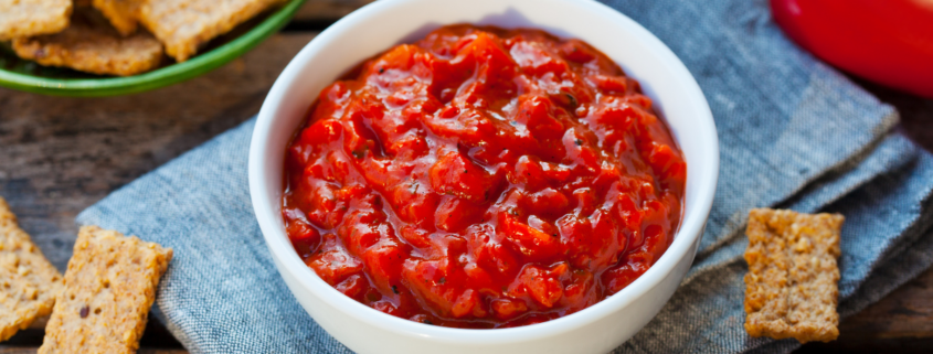 Sweet pepper and onion relish in a white bowl with crackers and fresh red bell peppers