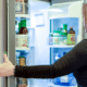 Woman opening refrigerator stocked with fresh food and condiments