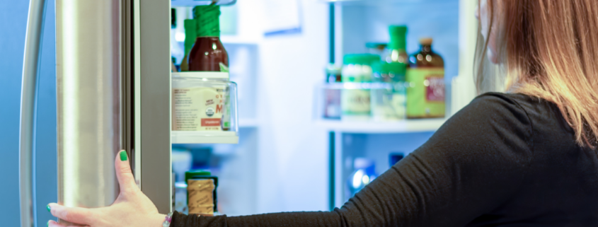 Woman opening refrigerator stocked with fresh food and condiments