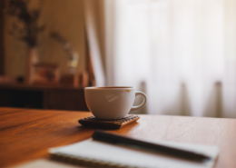 A cup of coffee, notebook, and pen on a table