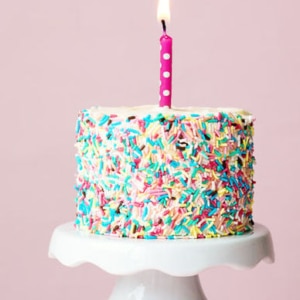 birthday cake on white stand with candle and sprinkles