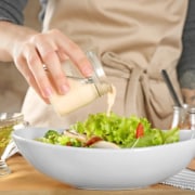 Woman adding tasty sauce to salad in dish on table