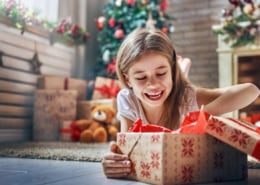 Cute little child opening present near Christmas tree