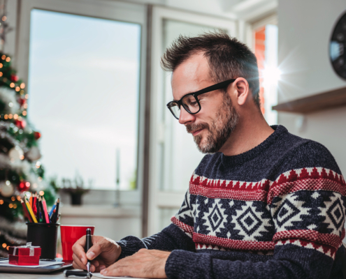 Dad Writing Family Christmas letter at desk with pen paper and laptop