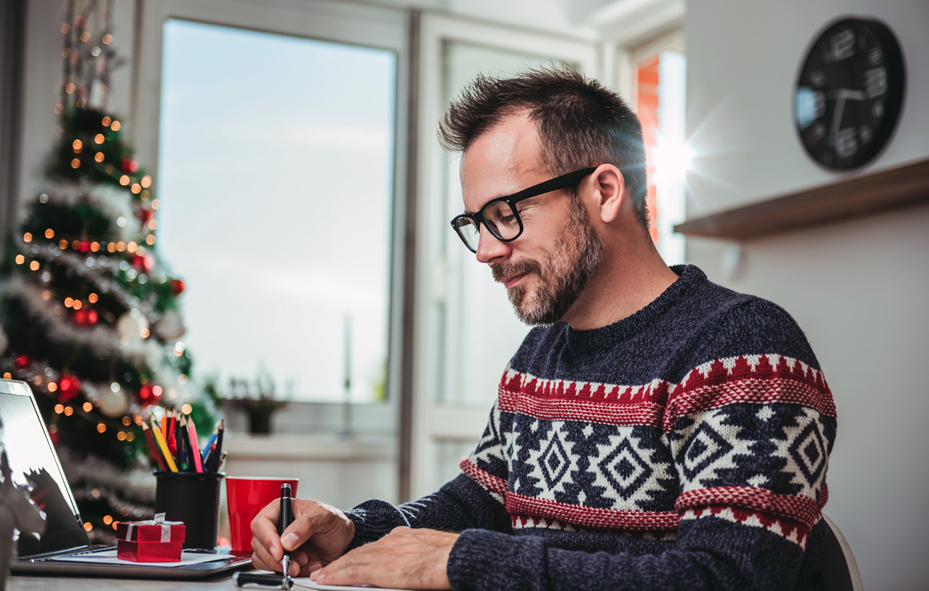 Dad Writing Family Christmas letter at desk with pen paper and laptop