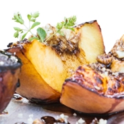 close up of grilled peaches with blue cheese and a balsamic reduction on a white background
