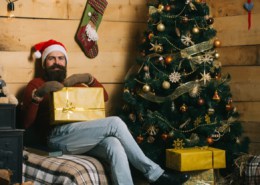 Happy bearded man sitting by Christmas tree with gift in hand