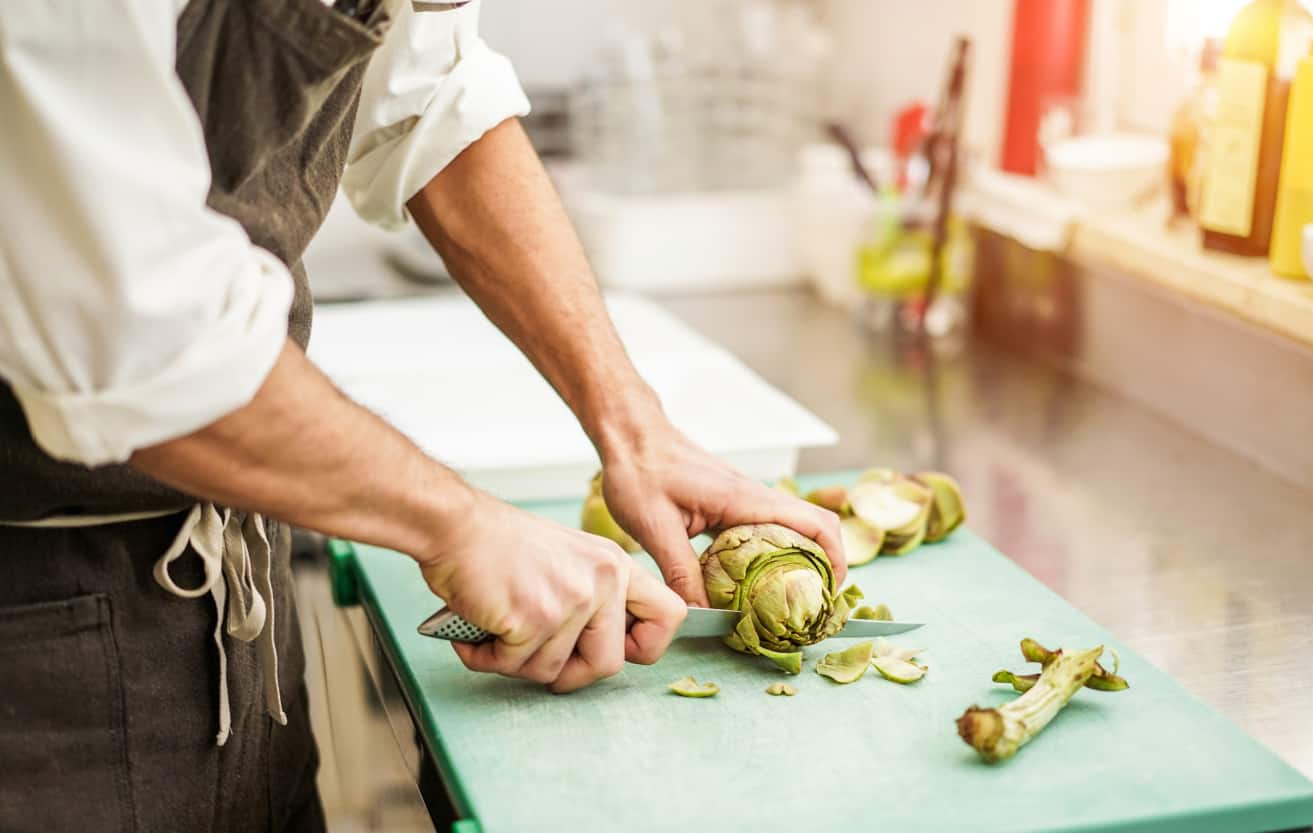 Chef cutting artichokes for dinner preparation - Man cooking inside restaurant kitchen - Focus on vegetable - Vegan cuisine, lifestyle and healthy food concept