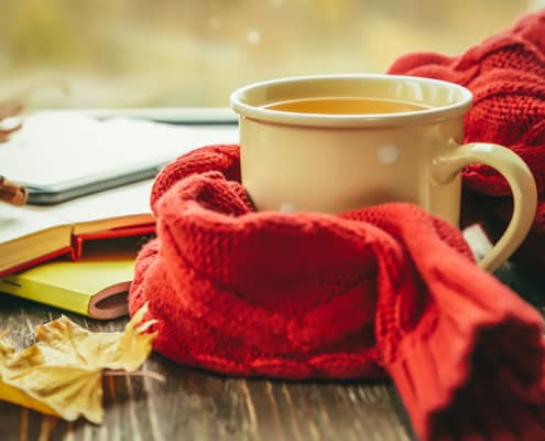 Autumn tea with scarf and leaves in front of window, copy space
