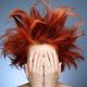 Redhead with messy hair covering her face with hands