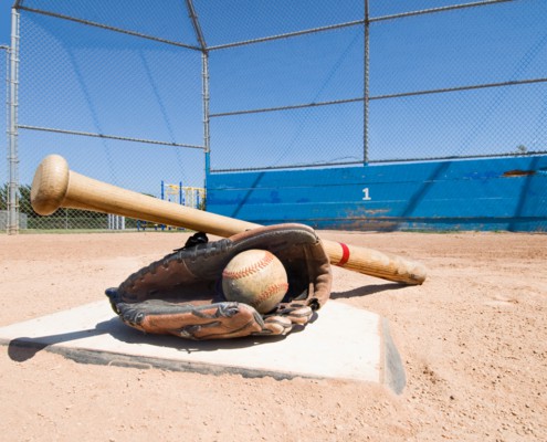 A baseball bat, glove and ball lie on top of home plate as a conceptual sports image.