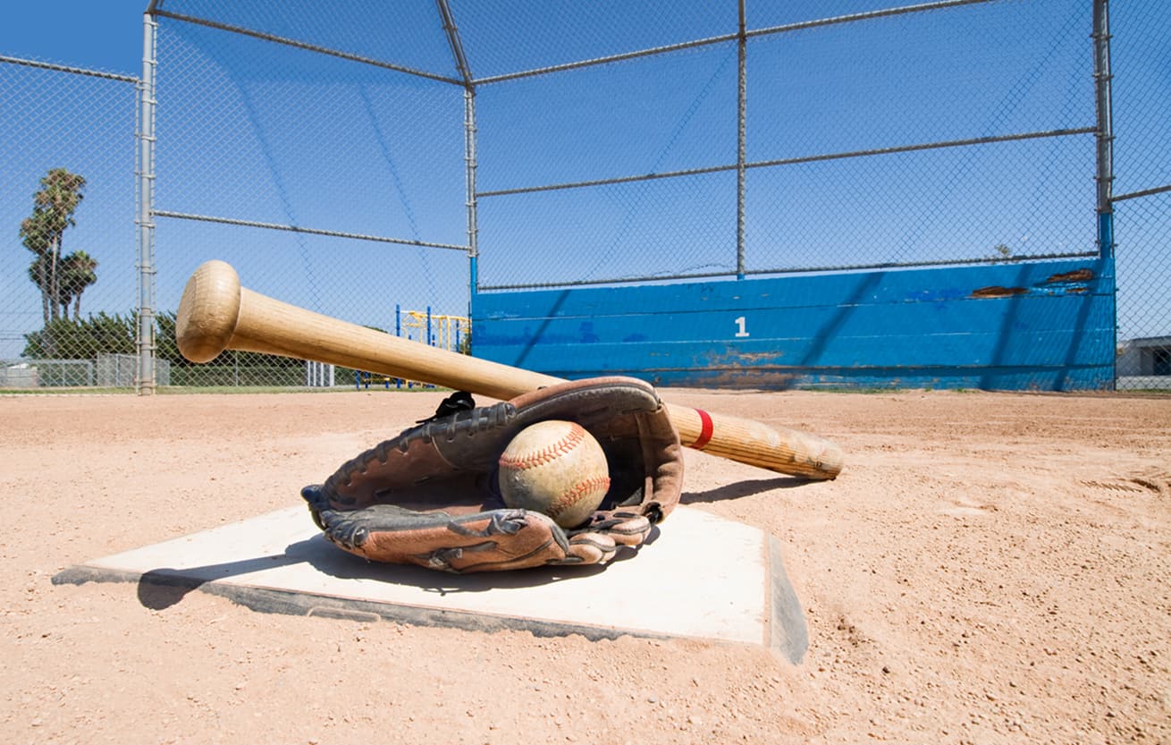 A baseball bat, glove and ball lie on top of home plate as a conceptual sports image.