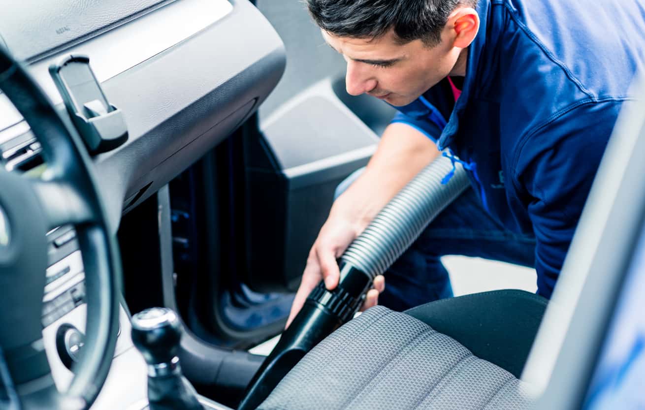 Young hard-working man using vacuum for cleaning the interior of a car at auto wash
