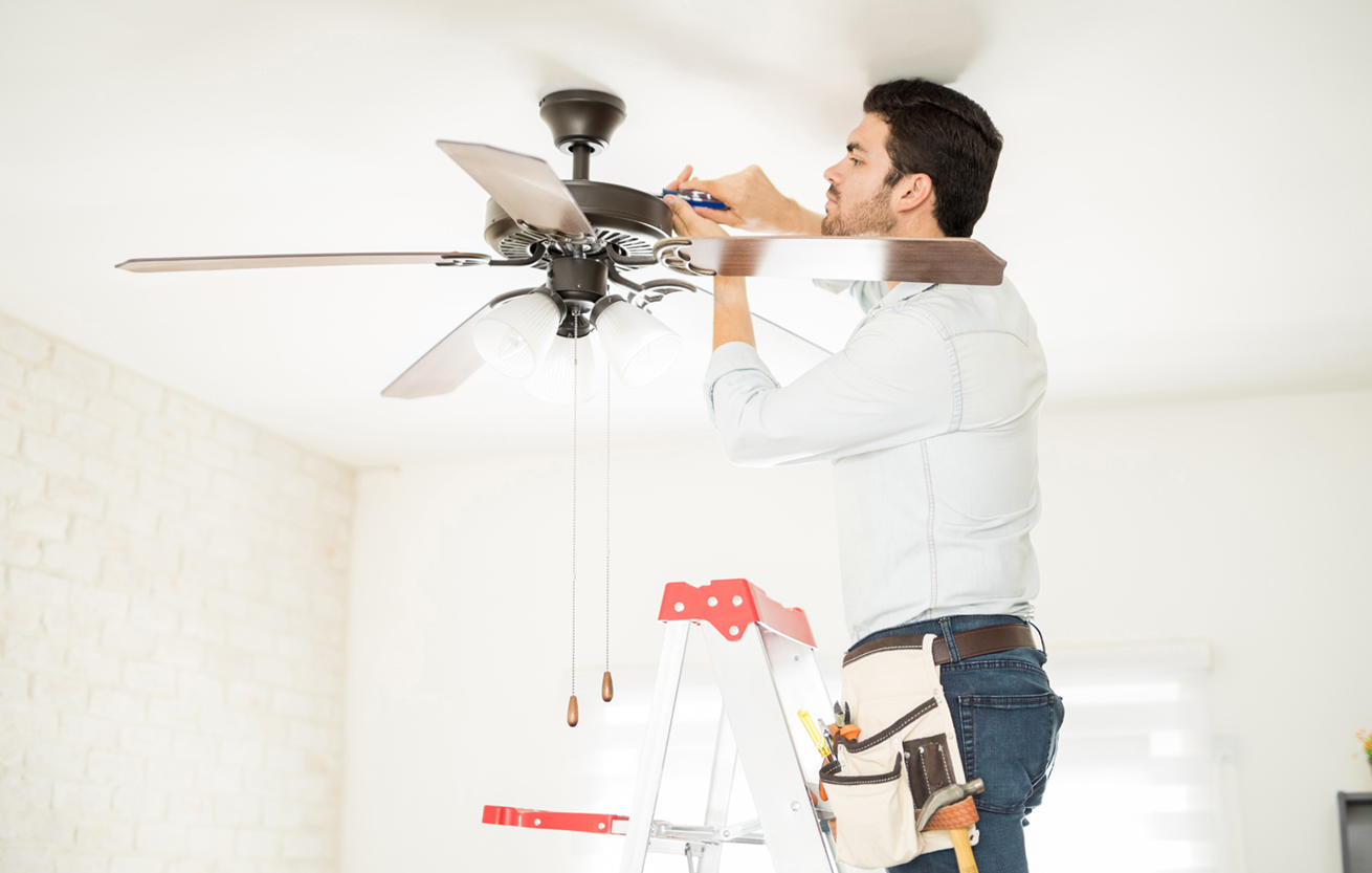 Attractive young handyman stepping on a ladder and fixing a ceiling fan