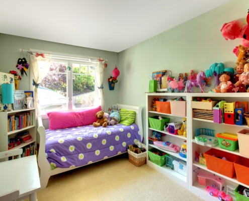 Girls bedroom with many toys and purple bed.